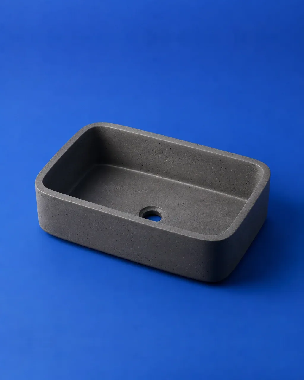 Lavamanos de sobreponer de concreto gris oscuro, de líneas simples, sobre fondo azul cobalto.