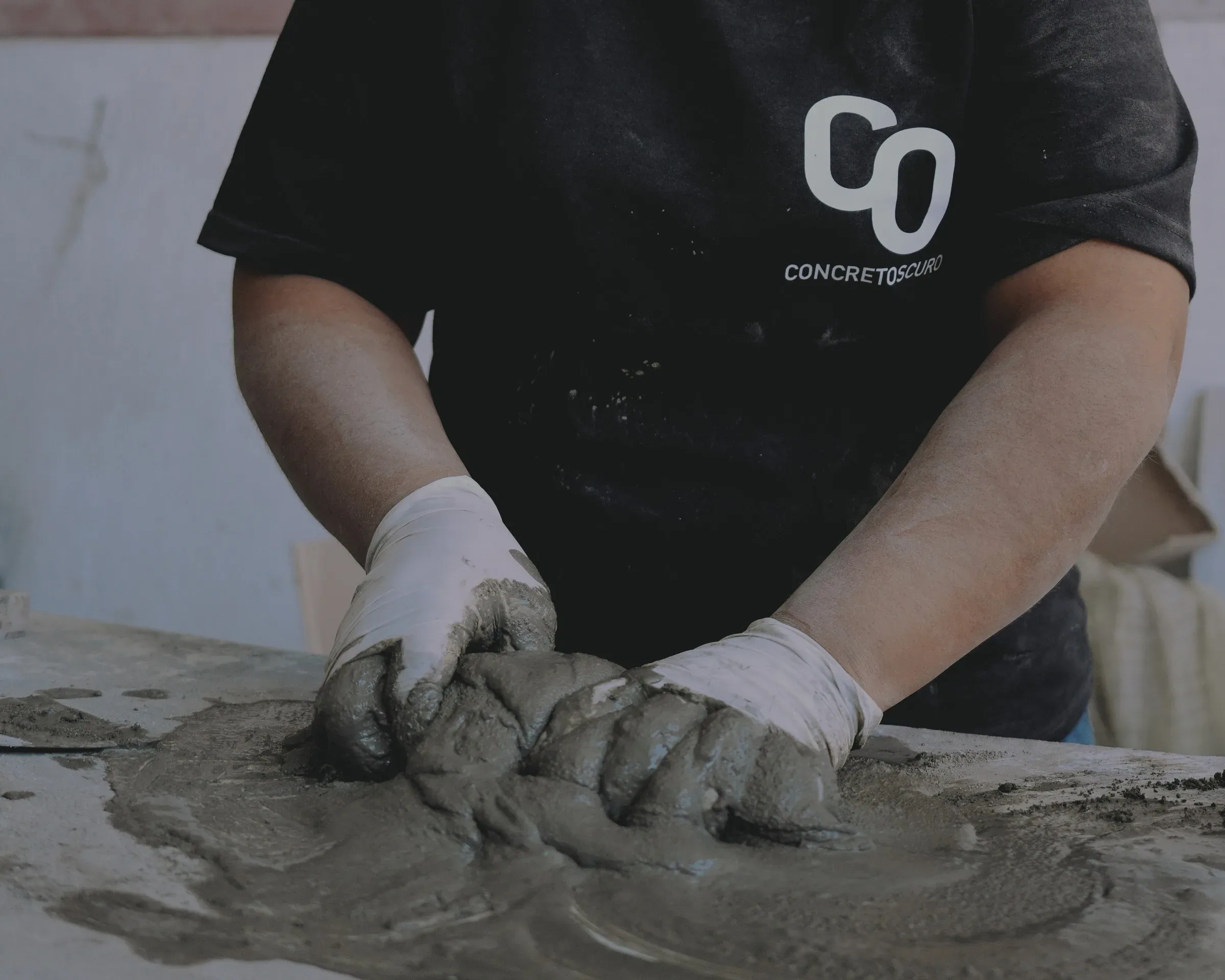 Manos con guantes trabajando una mezcla de concreto sobre una mesa.